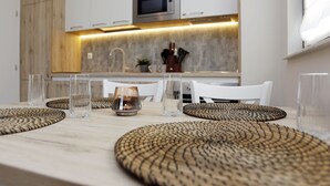 Une cuisine moderne avec des meubles blancs, un four à micro-ondes et un coin repas agrémenté d’une table où sont disposés des verres transparents et des sets de table en fibres tressées.