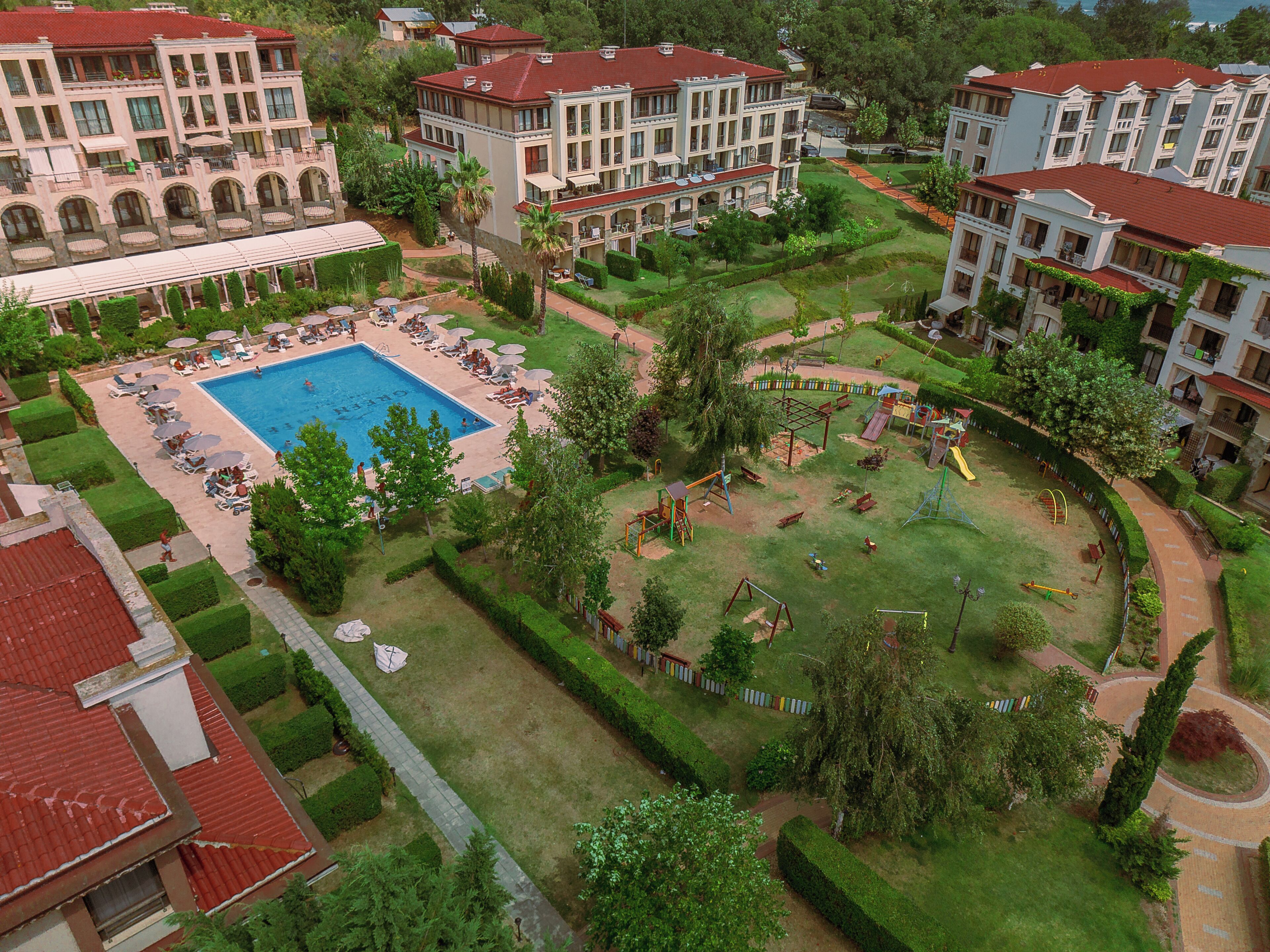 A large swimming pool surrounded by lounge chairs and umbrellas, with a playground nearby.
