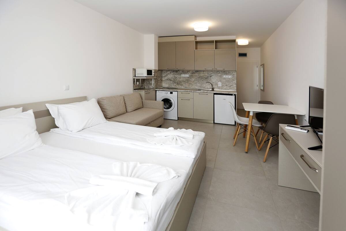 Una habitación de hotel con cama, sofá, escritorio, lavadora y kitchenette.