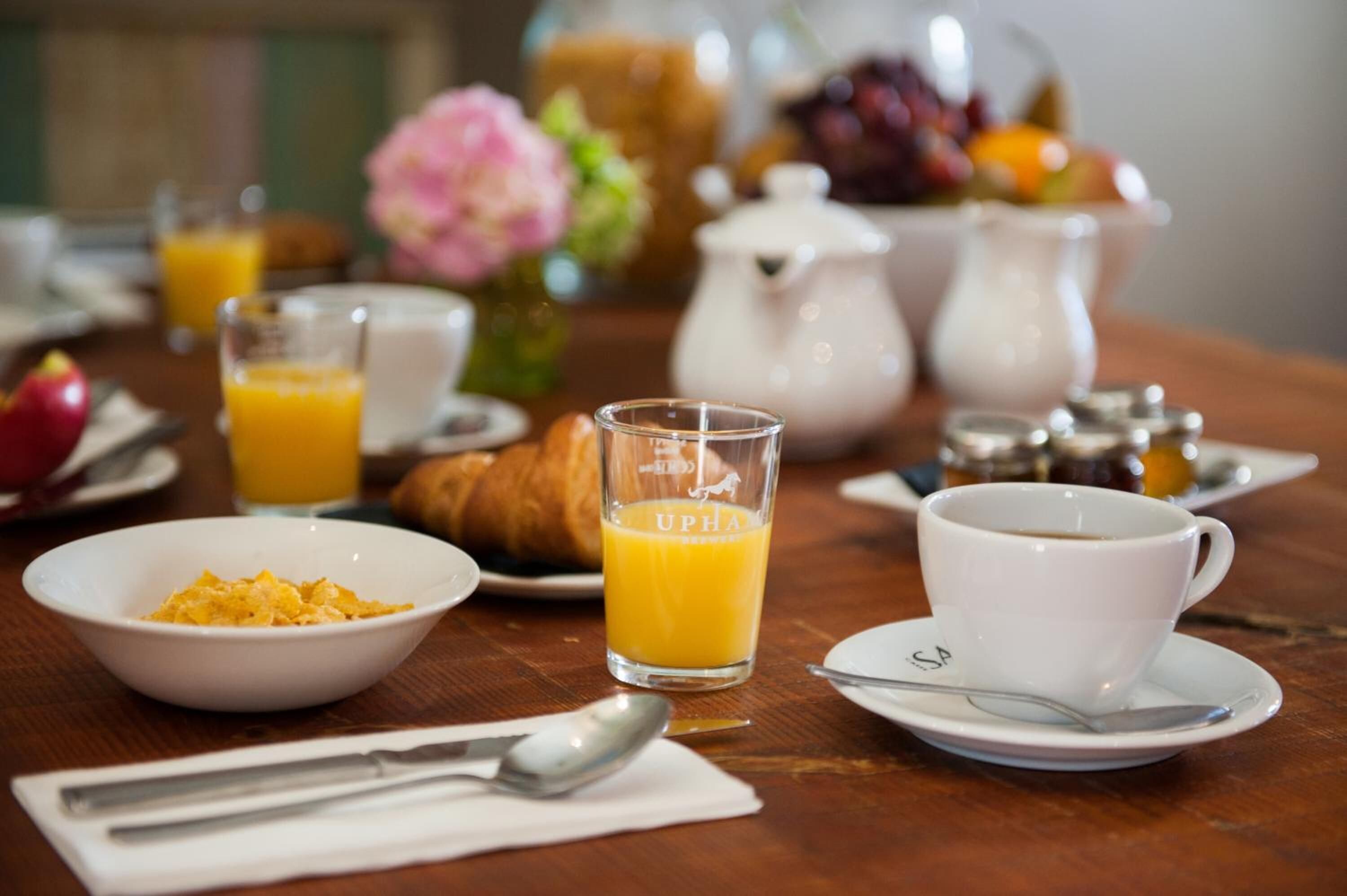 Un desayuno con un croissant, jugo de naranja, café y un tazón de cereal.