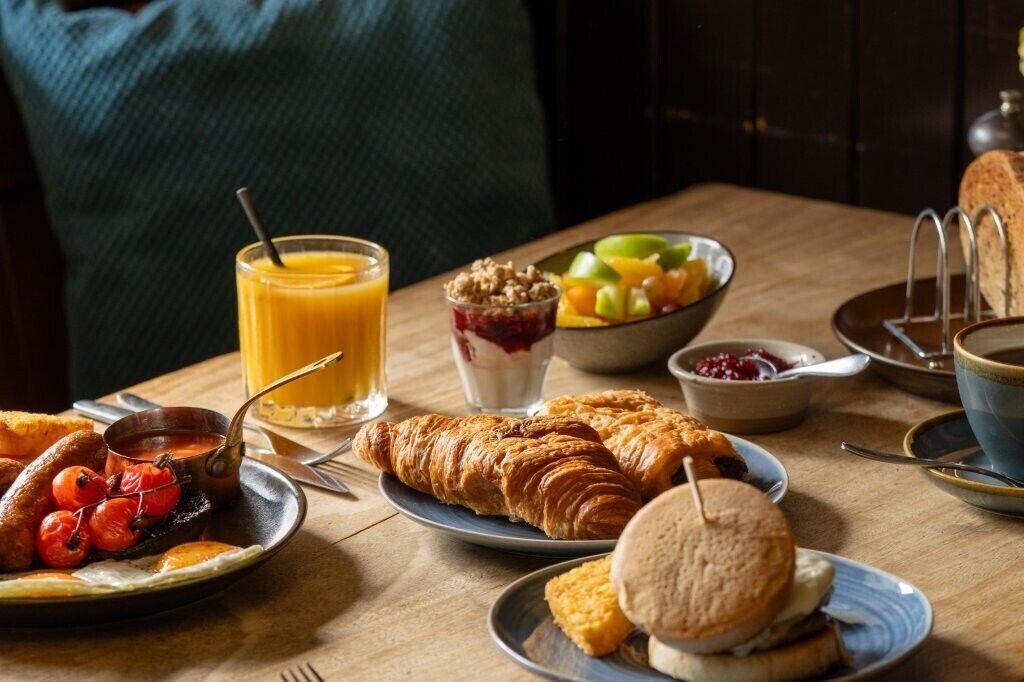 A breakfast table with croissants, muffins, and a fruit bowl.