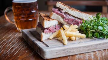 Un sandwich accompagné de frites et d’un verre de bière, le tout servi sur une planche en bois.
