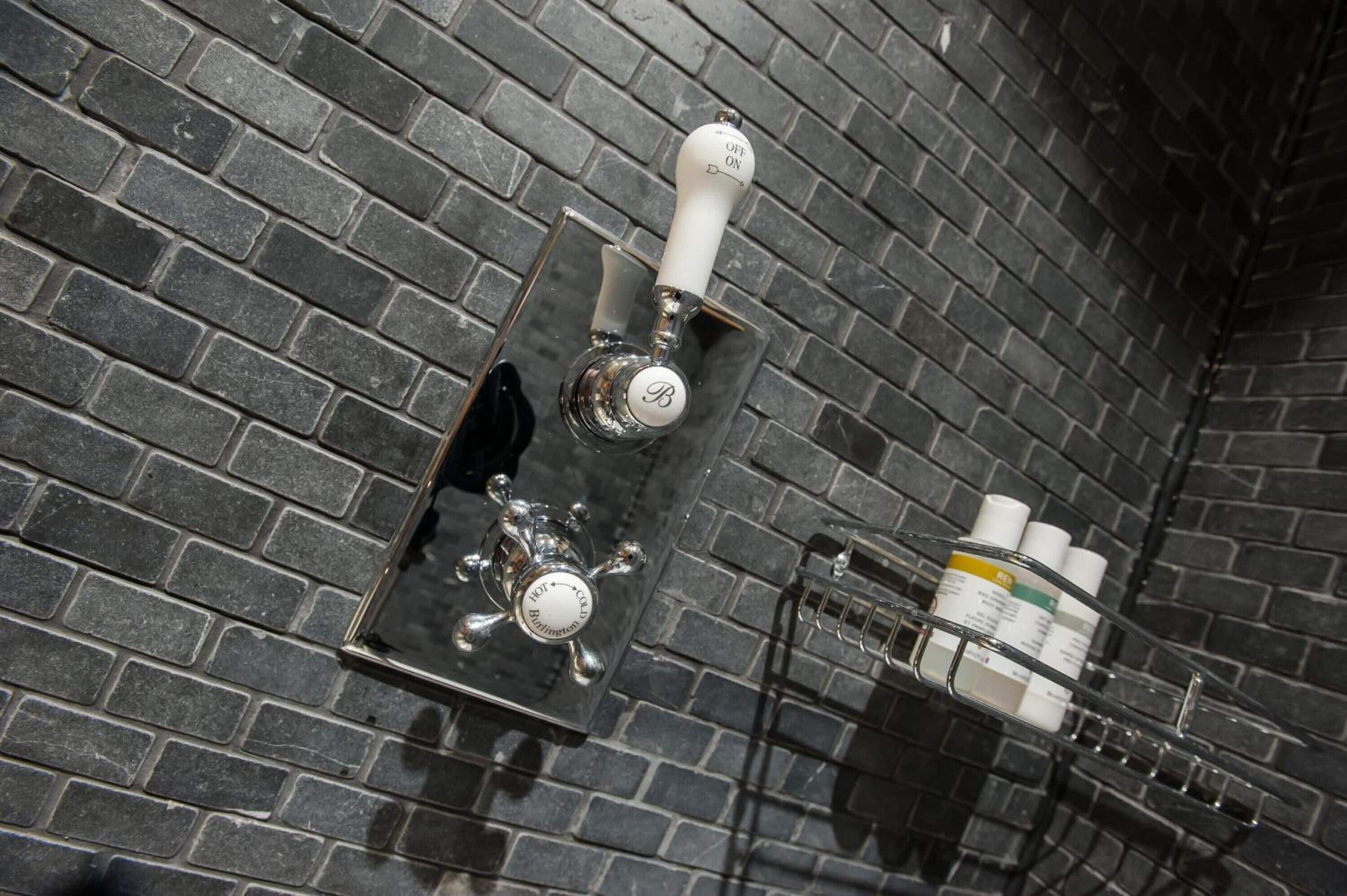 A bathroom with a black brick wall, a chrome faucet, and a shelf with toiletries.