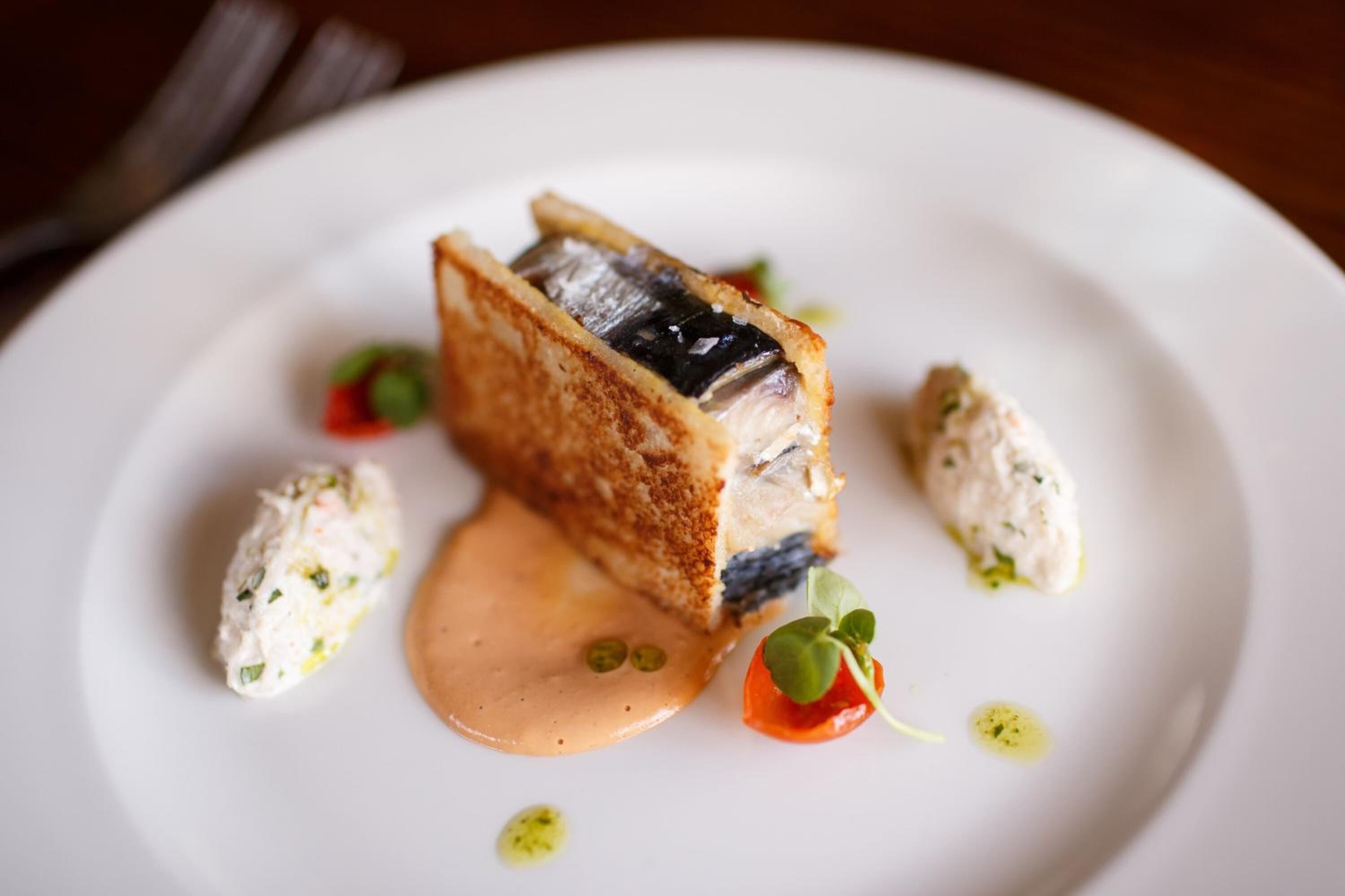 Een bord met een gepaneerde vis, romige saus en garneringen.