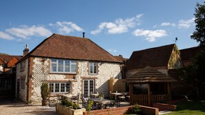 A stone building with a tiled roof, outdoor seating area, and a thatched-roof gazebo. - The White Hart, South Harting (Petersfield)