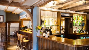 A bar area with wooden beams, stools, and a variety of liquor bottles. - The White Hart, South Harting (Petersfield)