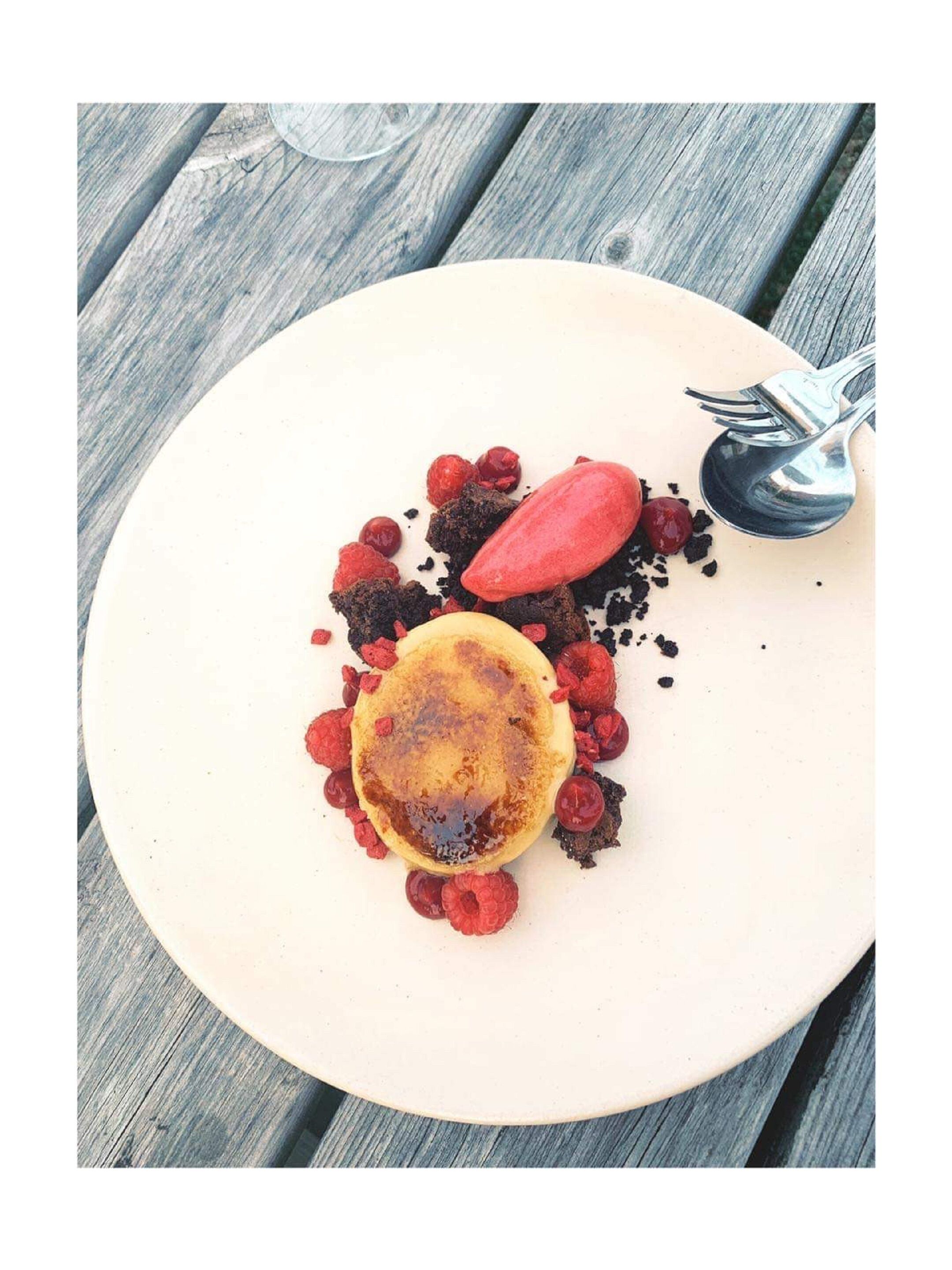 A round plate with pancakes, raspberries, and chocolate shavings on a wooden table.