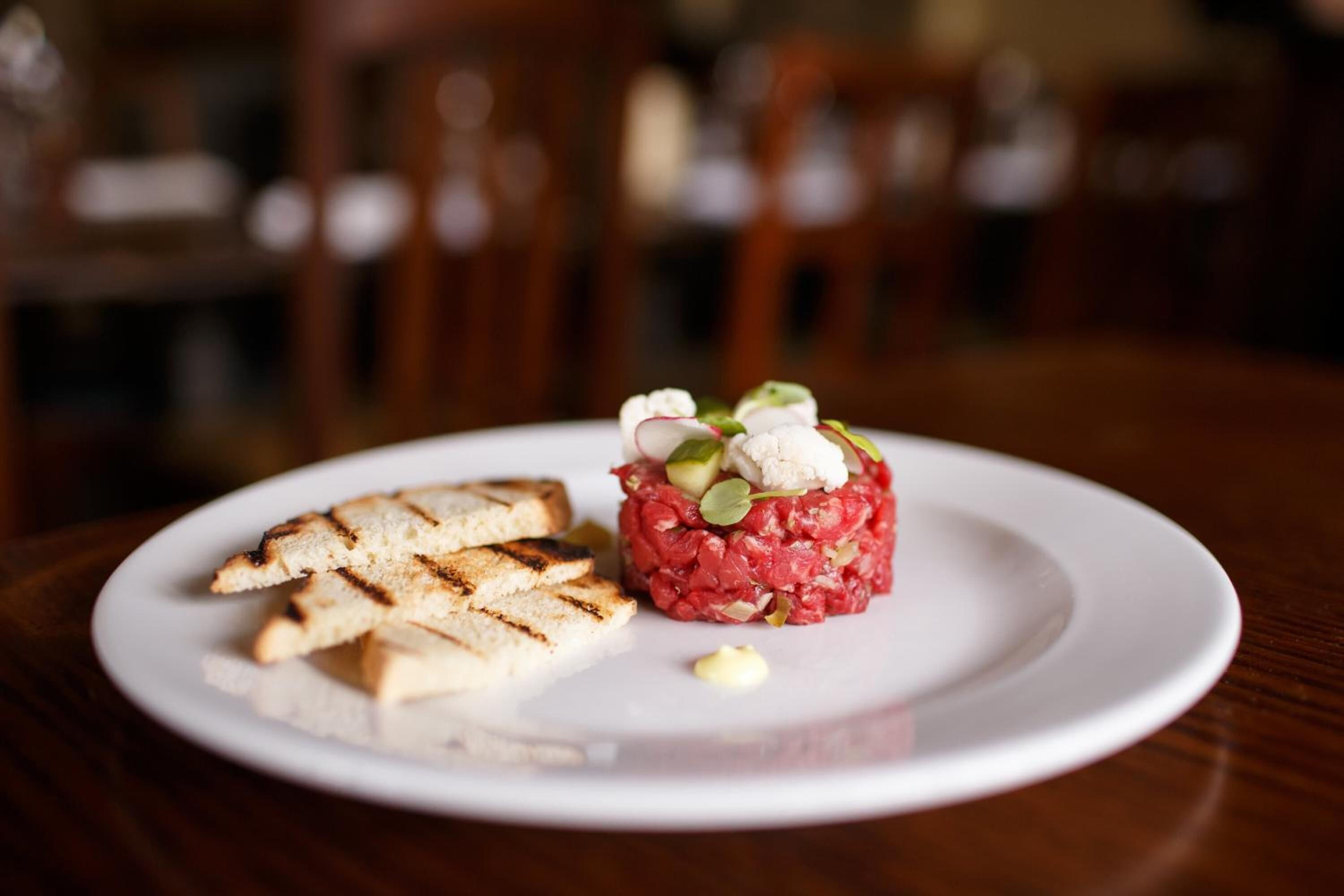 A plate with steak tartare and grilled bread on a wooden table.