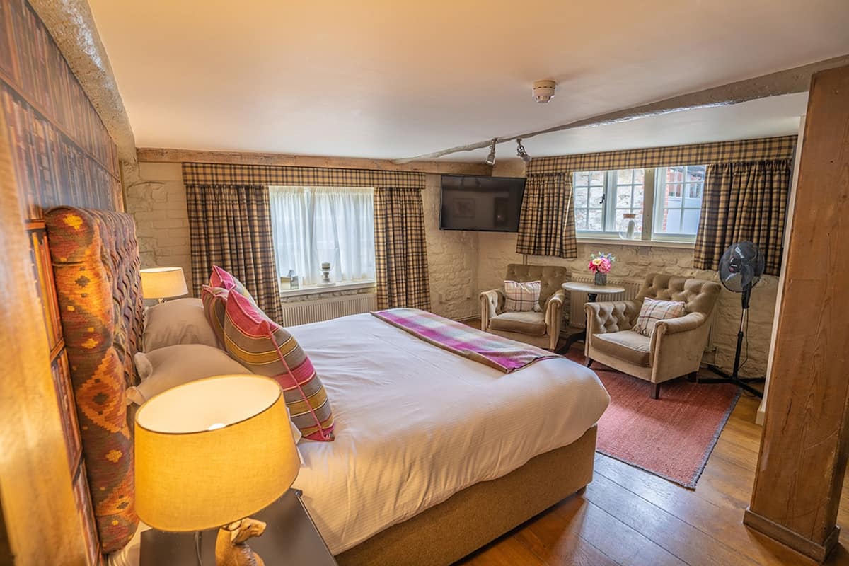 A bedroom with a large bed, a chair, a small table, and a TV mounted on the wall.