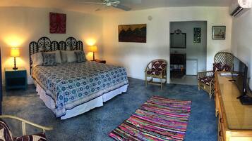 A bedroom with a bed, two bedside lamps, a ceiling fan, a colorful rug, and a dresser.
