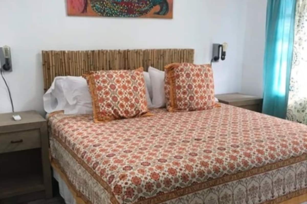 Cama bem arrumada com roupa de cama estampada, mesa de cabeceira e luminária fixada na parede.