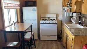A compact kitchen with wooden walls, a white stove, a refrigerator, and a sink. - South Fork Lodge & RV Park (South Fork)