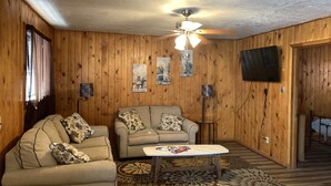A cozy living room with wooden walls, a ceiling fan, a flat-screen TV, two sofas with patterned cushions, a coffee table, and a patterned rug. - South Fork Lodge & RV Park (South Fork)