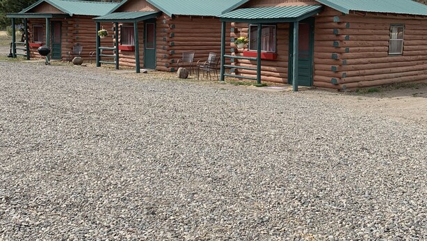 A row of log cabins with green roofs, gravel ground, and a mountainous backdrop. - South Fork Lodge & RV Park (South Fork)