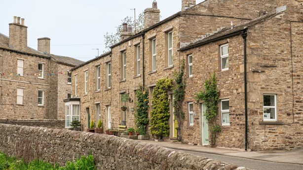 A row of stone buildings with uniform windows and doors, a stone wall in the foreground, and some greenery around the buildings. - Milton House Studio Apartment Suites (Leyburn)