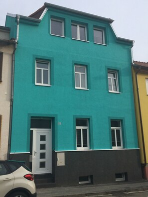 A multi-story building with a teal facade, white-framed windows, and a white door.