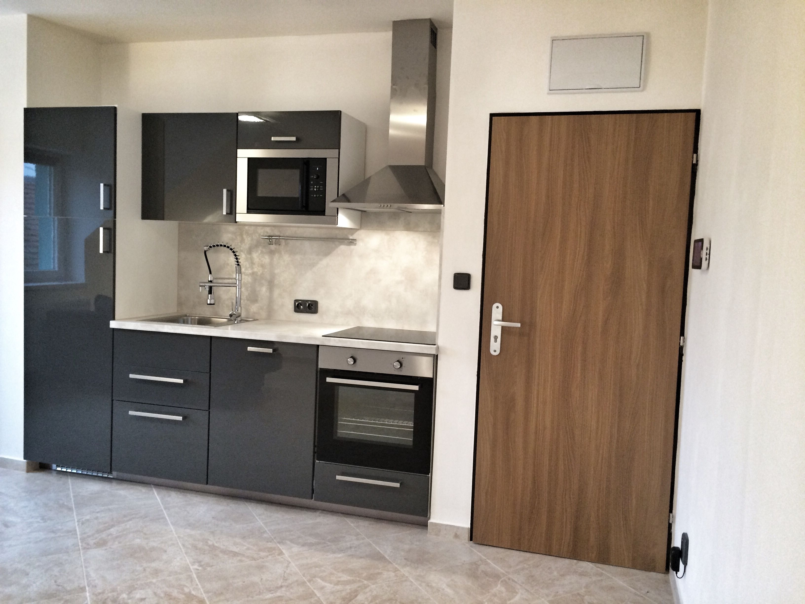 A modern kitchen with dark cabinetry, a stainless steel microwave, a built-in oven, and a wooden door.