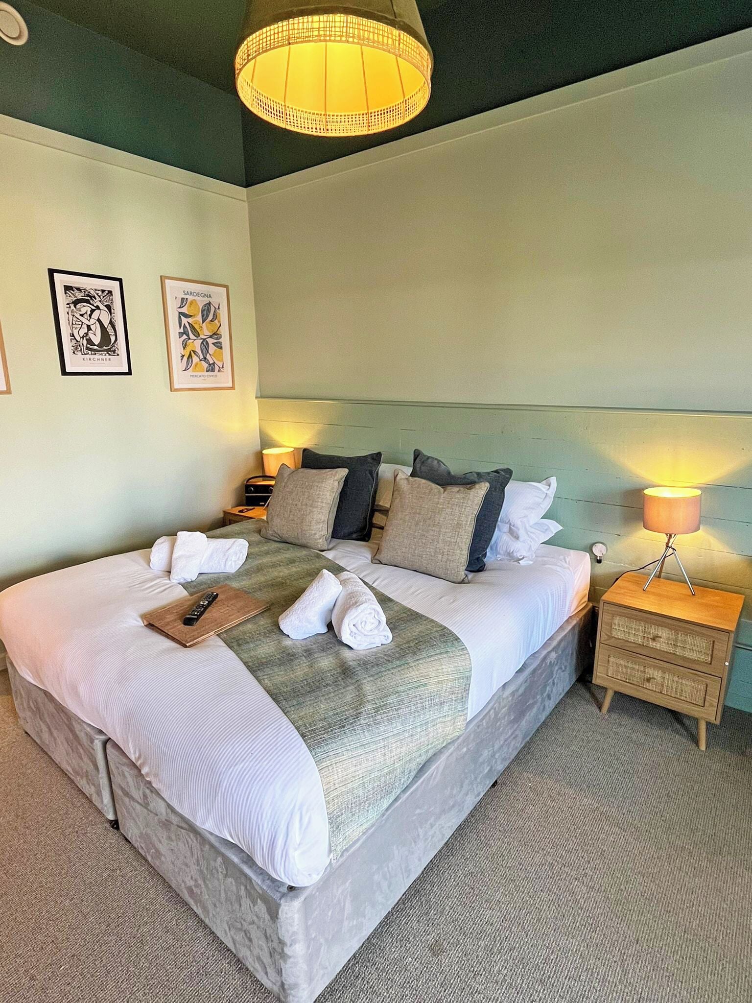 A neatly made bed with pillows and towels, a bedside lamp, and framed artwork on the wall.
