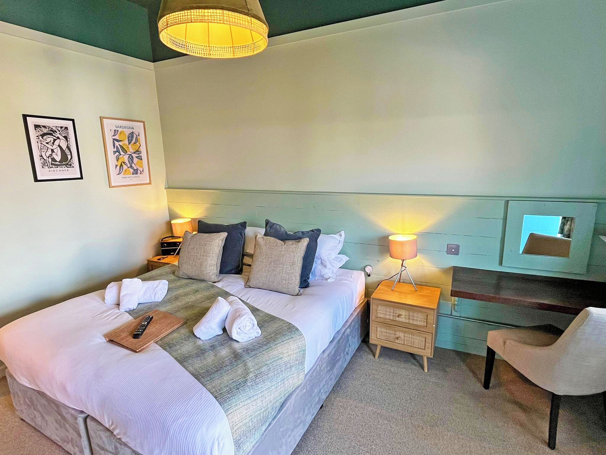 Ein Hotelzimmer mit Bett, Nachttischen, einem Sessel, einer Lampe und Bildern an der Wand.