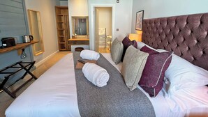 A hotel room with a large bed, a wooden shelf, a mirror, a wardrobe, and a hanging light fixture. - The Running Horse (Winchester)