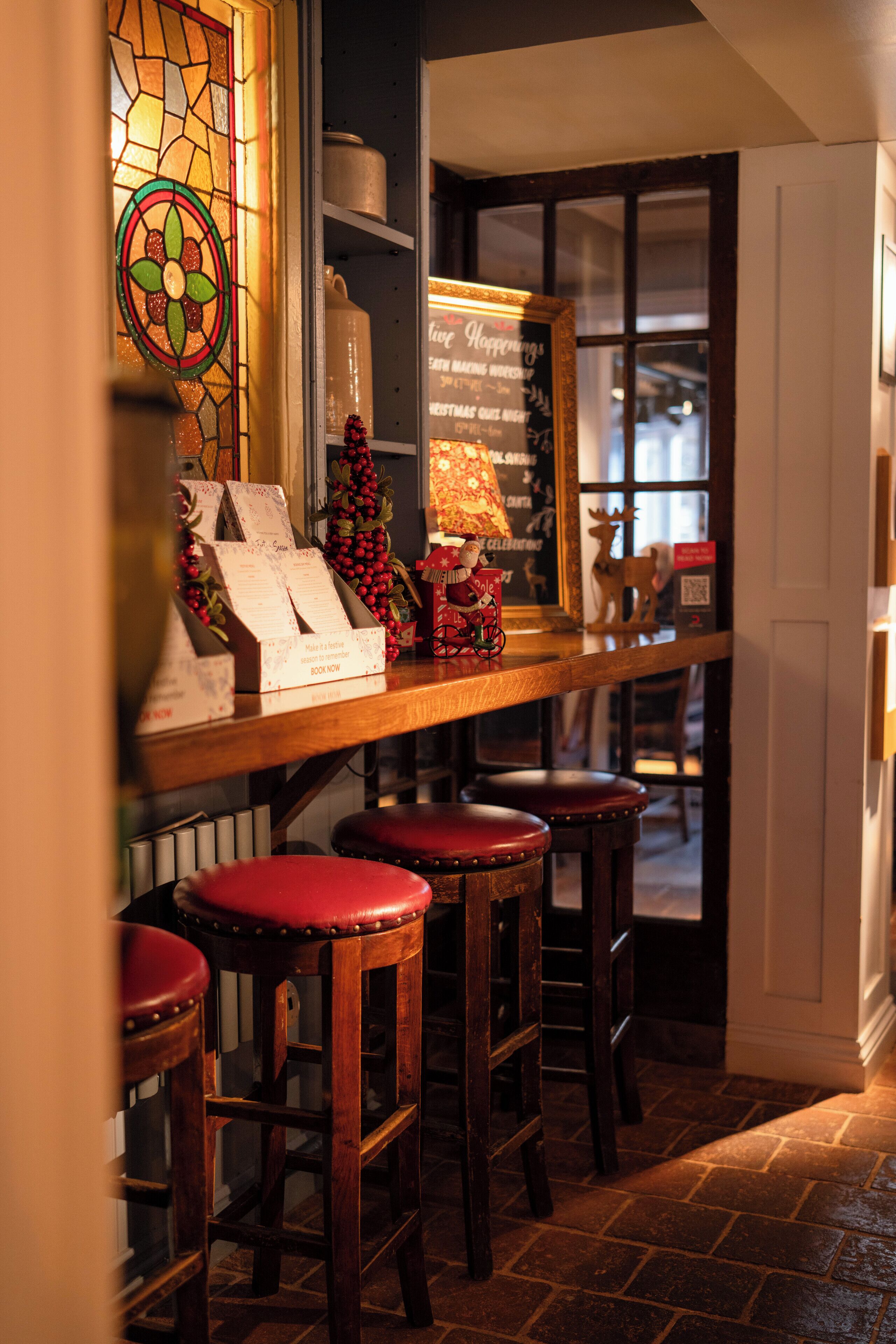A cozy bar area with wooden stools, a stained glass window, and a chalkboard menu.