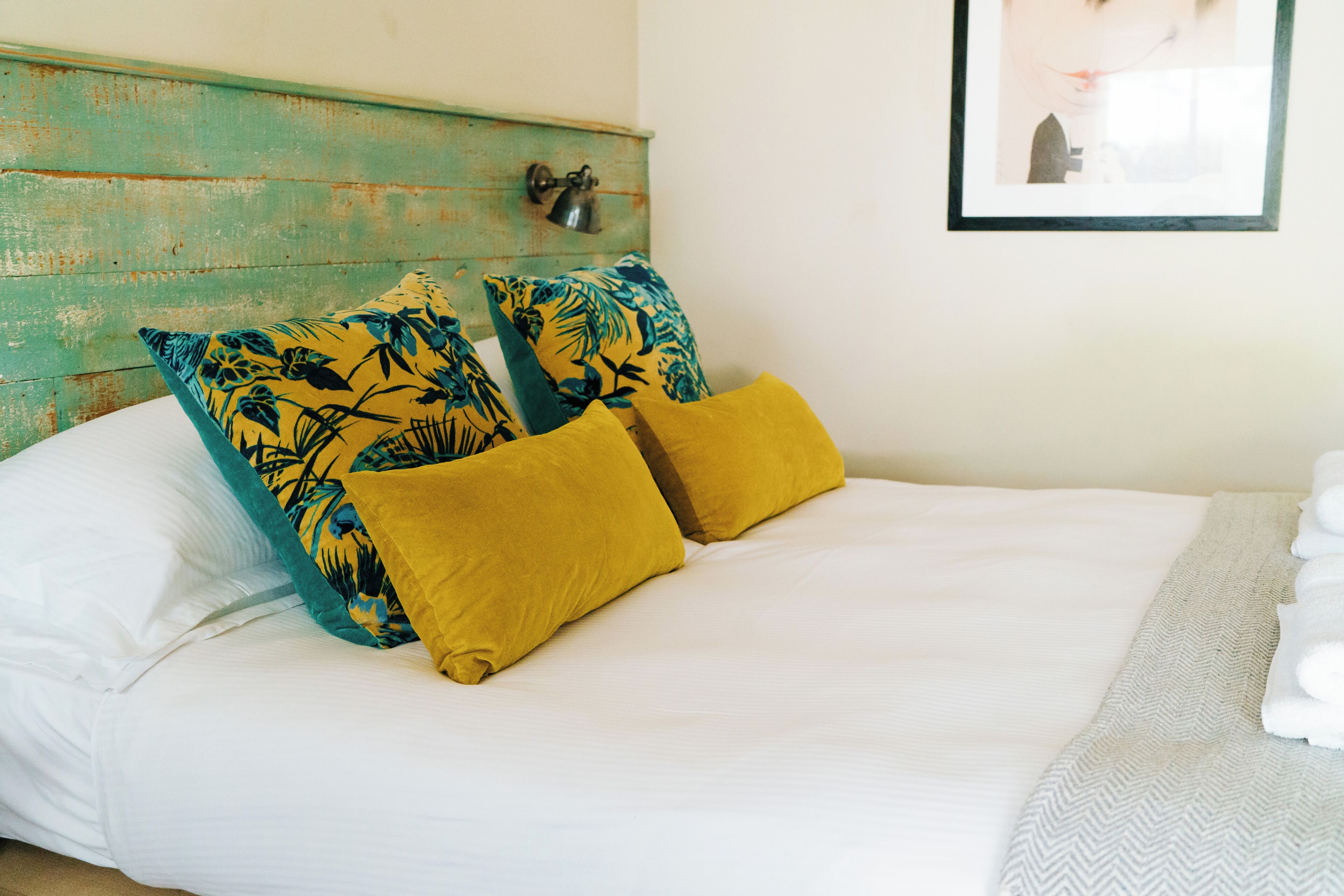 A bed with white linens, two yellow pillows, and a teal and black floral pillow.