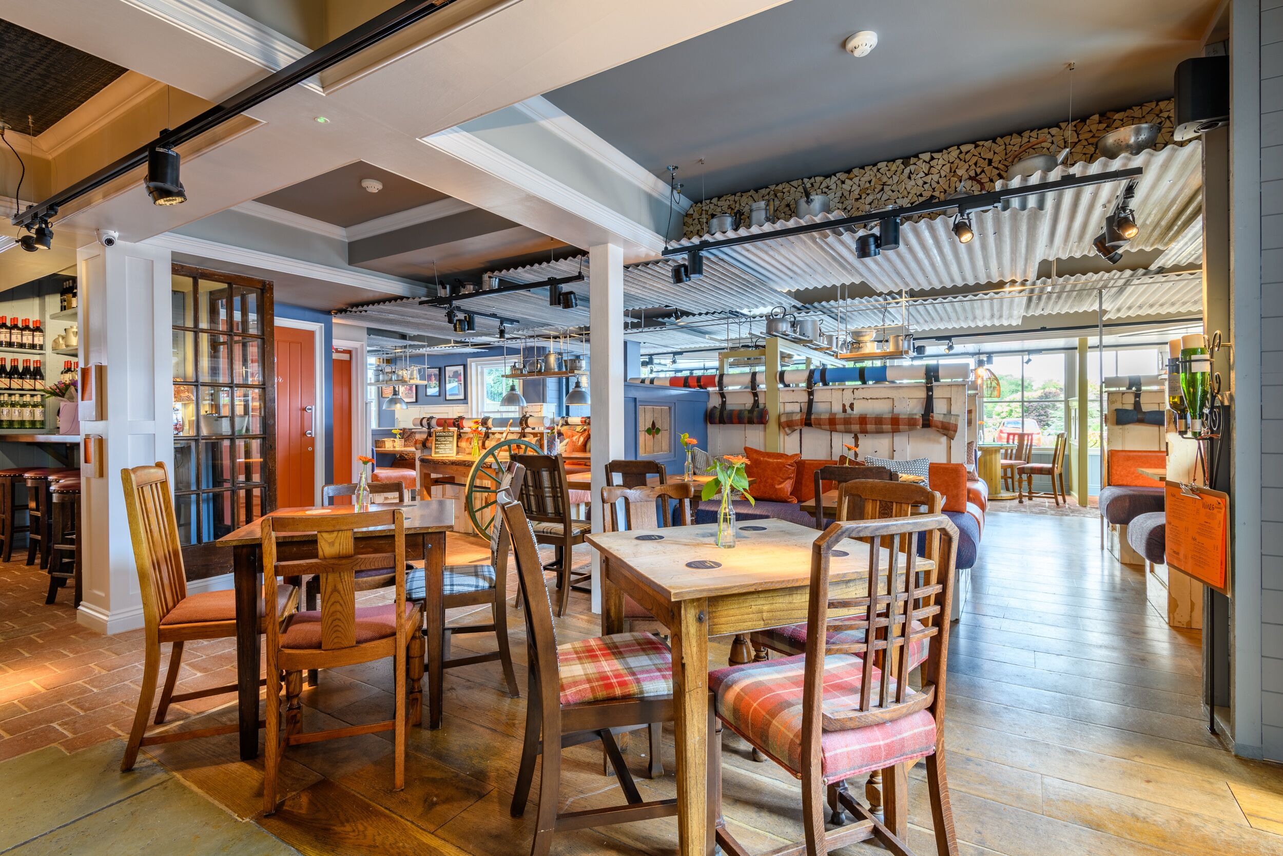 Un restaurante espacioso con mesas y sillas de madera, una zona de bar con estantes llenos de botellas, y una cocina visible a través de una puerta abierta.