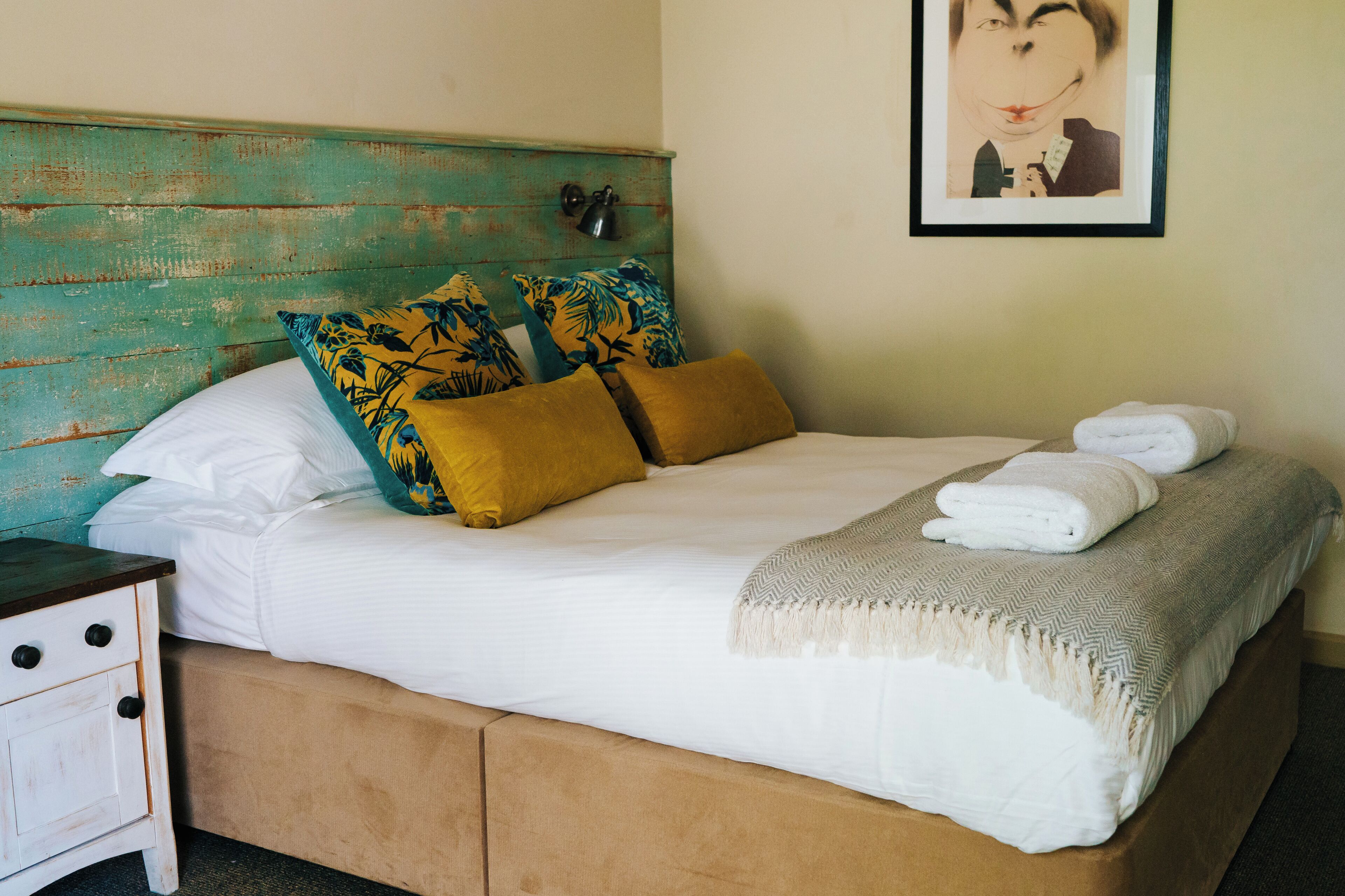 A neatly made bed with white linens, two mustard-colored pillows, and a white throw blanket.