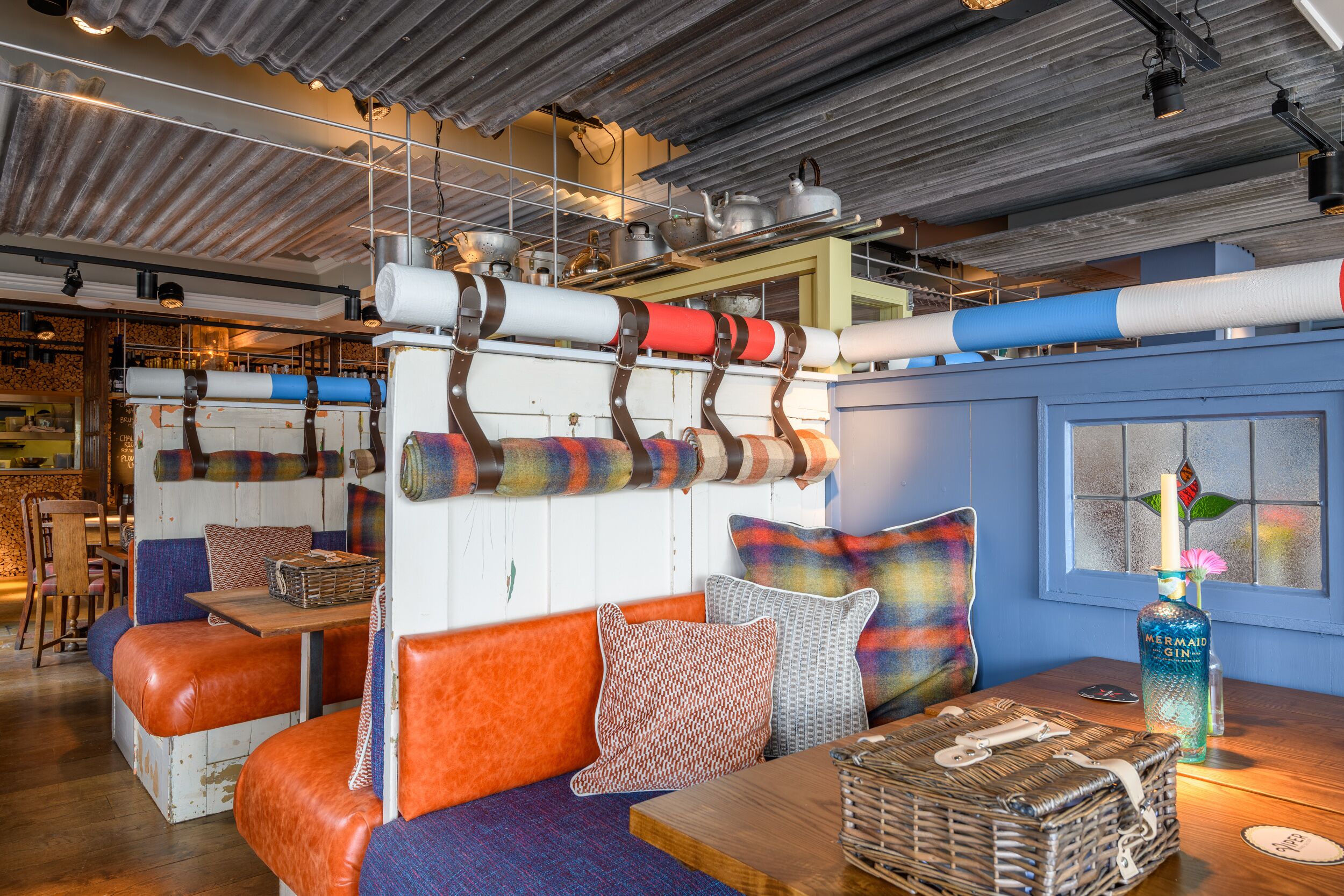 A cozy seating area with cushioned benches, a wicker basket, and a bottle of gin on a wooden table.