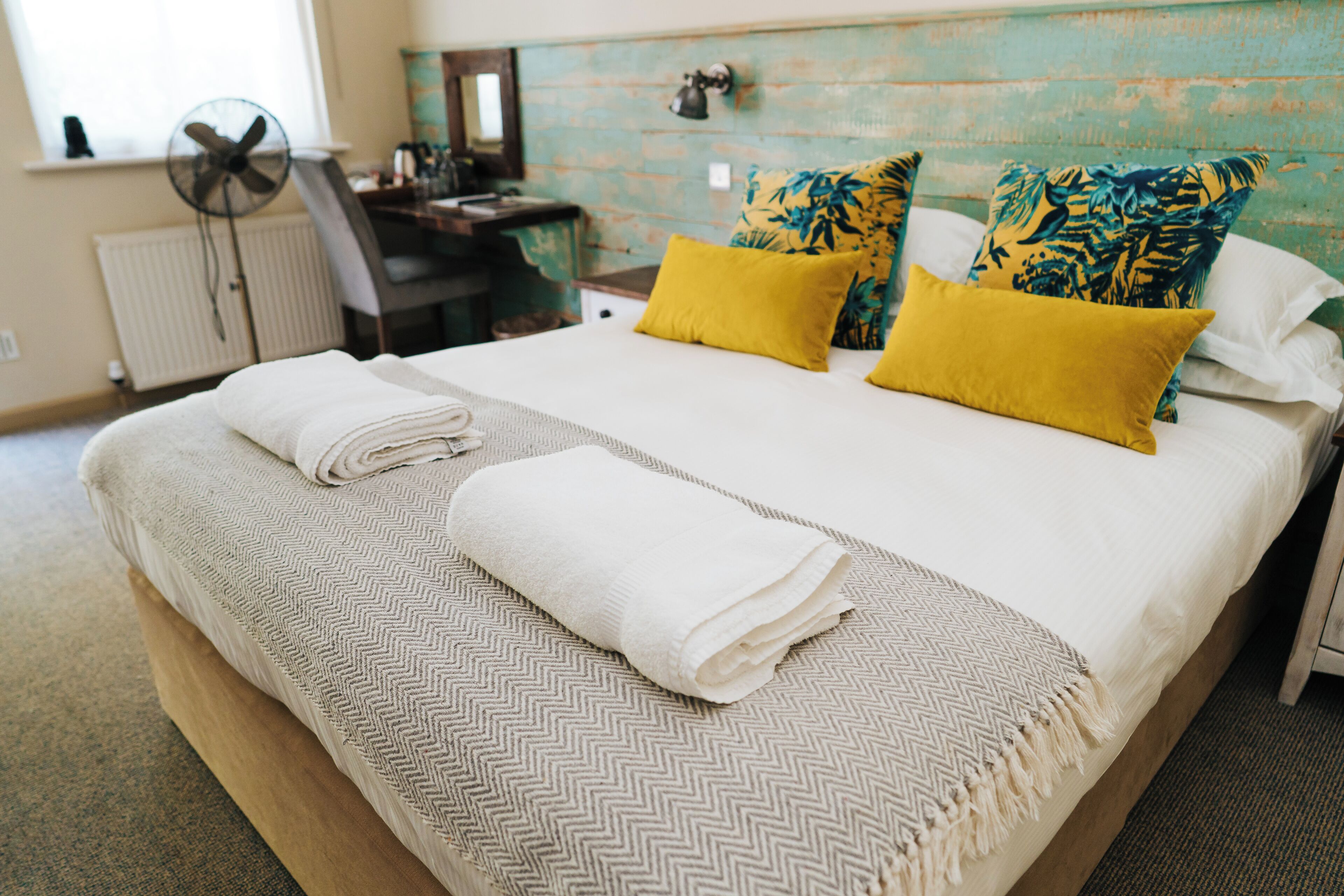 Una cama bien hecha con una colcha de diseño greca, dos almohadas amarillas y una manta blanca.