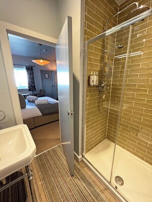 A hotel bathroom with a shower, a sink, and a bed in the adjacent room. - The Running Horse (Winchester)