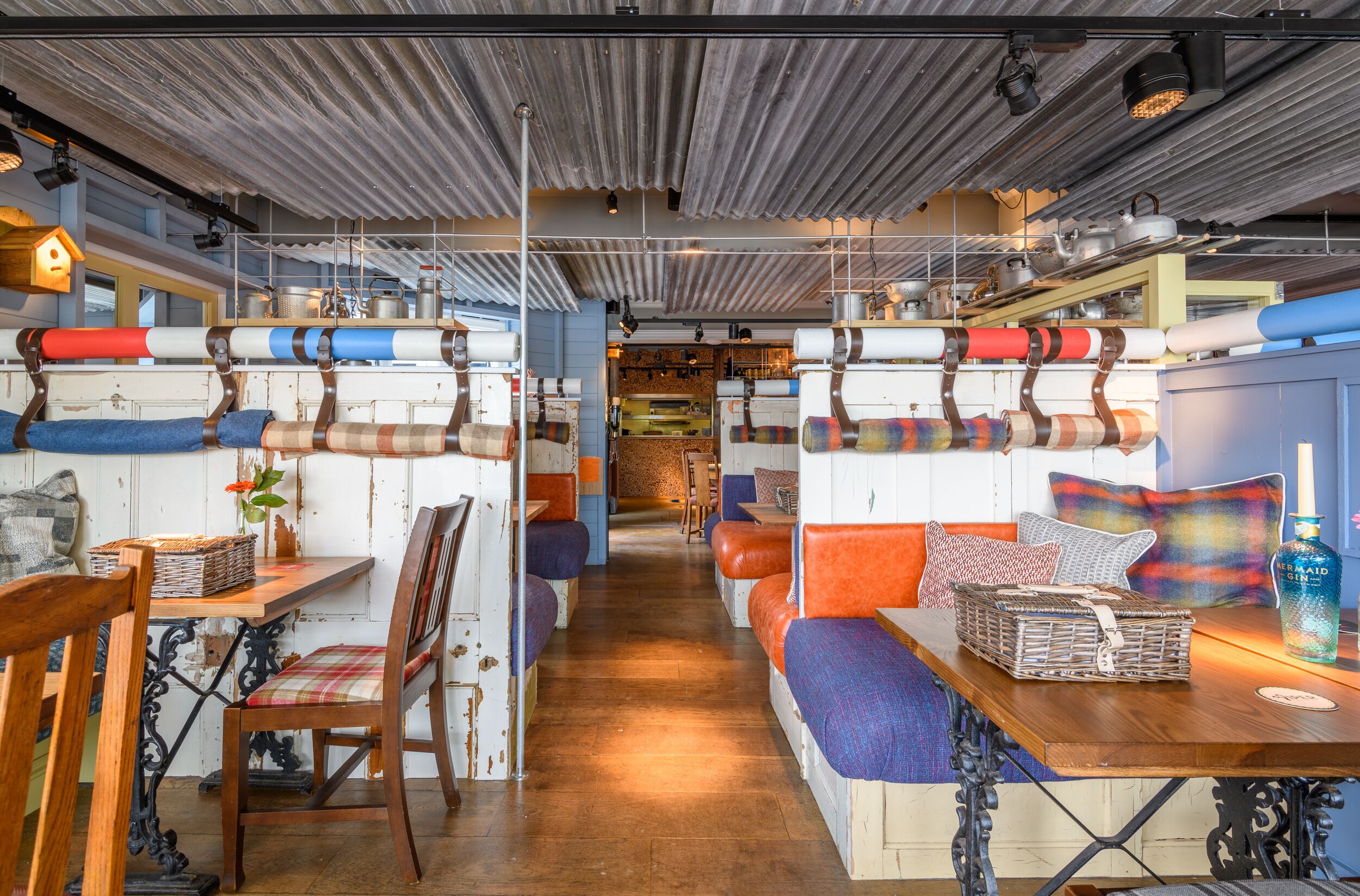A cozy restaurant with wooden tables and benches, a kitchen area in the background, and a rustic ceiling.