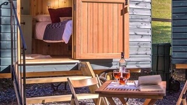 A cozy cabin with a wooden interior, a bed with pillows, a table with a bottle and glasses, and a view of the outdoors. - Siabod Huts (Llanrwst)