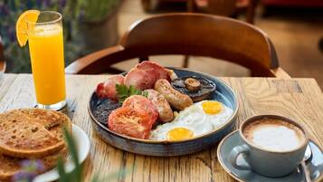 A breakfast plate with eggs, sausages, mushrooms, and toast, a glass of orange juice, and a cup of coffee on a wooden table.