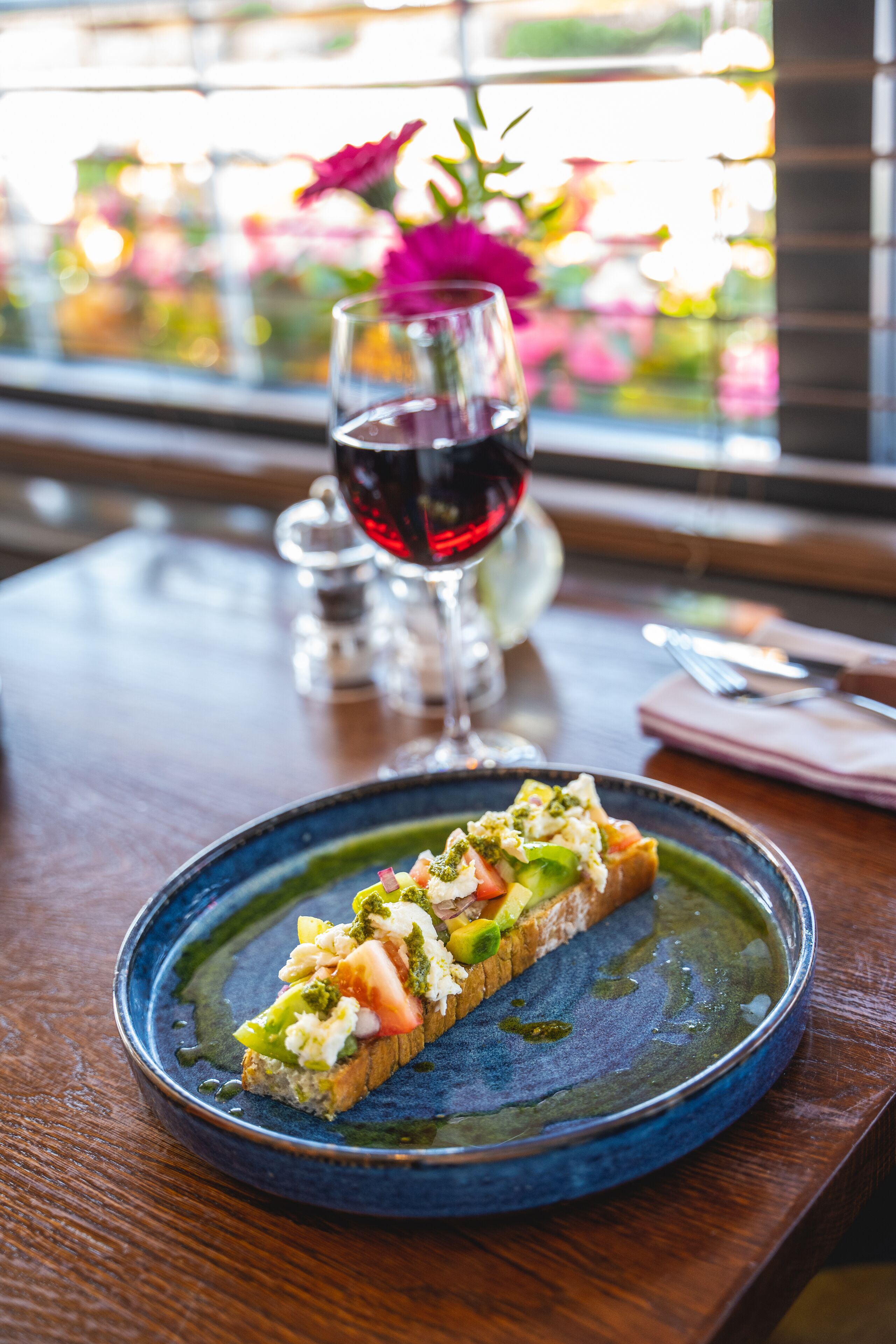 A dining table with a plate of food, a glass of red wine, and a vase with flowers.