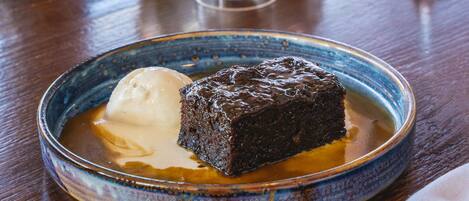Un plato de postre con un pastel de chocolate y helado, una copa de vino tinto y un jarrón con flores sobre una mesa de madera.