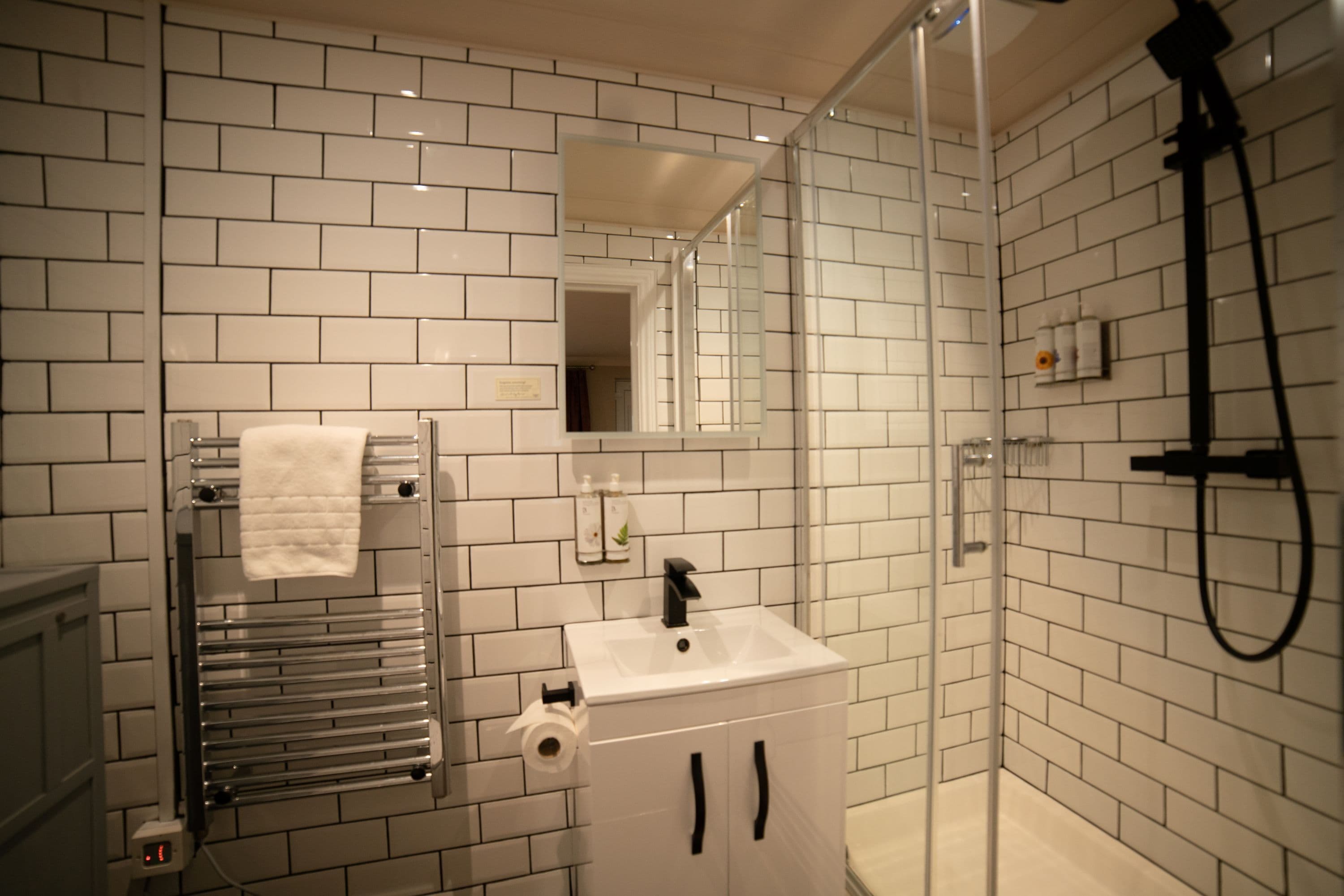 A modern bathroom with white subway tiles, a glass-enclosed shower, a white sink, and a towel rack.