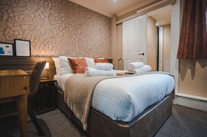 Un dormitorio ordenado con una cama grande, una mesita de noche, una silla y una pared con estampado floral.