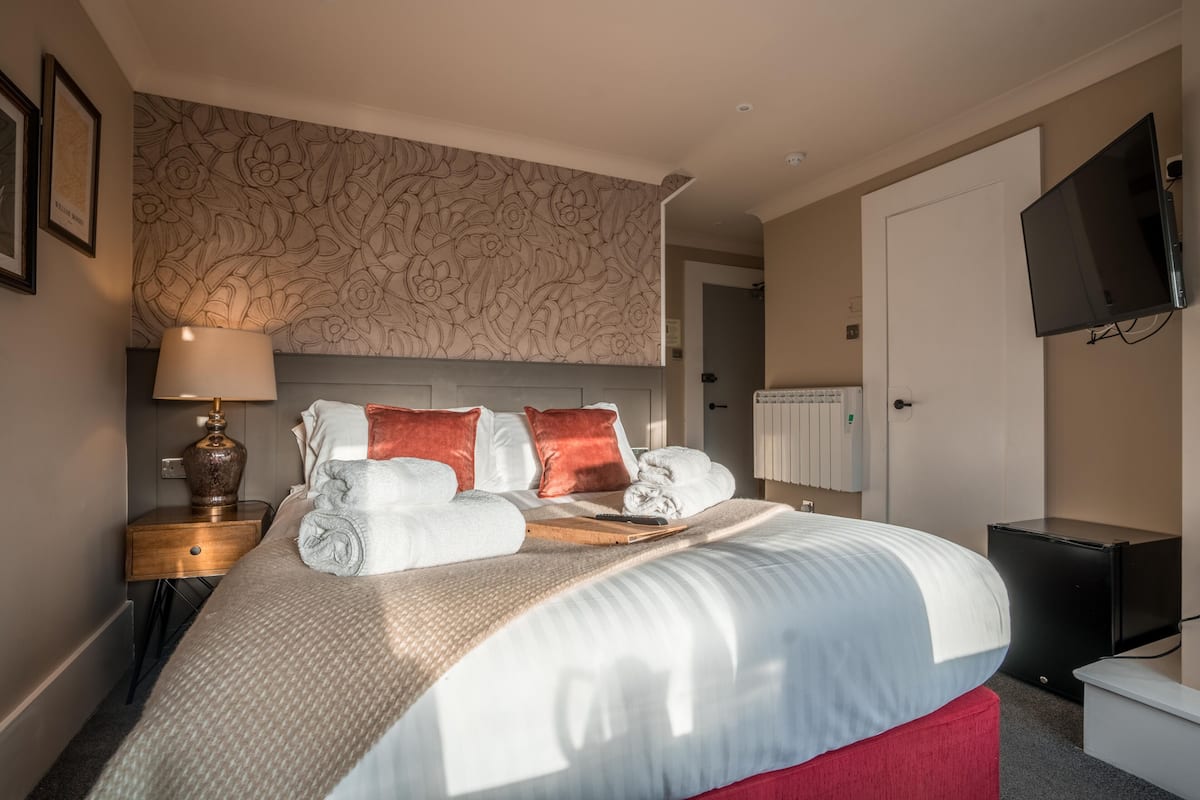 A neatly made bed with a patterned headboard, a bedside lamp, and a flat-screen TV mounted on the wall.