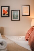Una habitación de hotel con una cama, un almohadón y tres cuadros enmarcados en la pared.