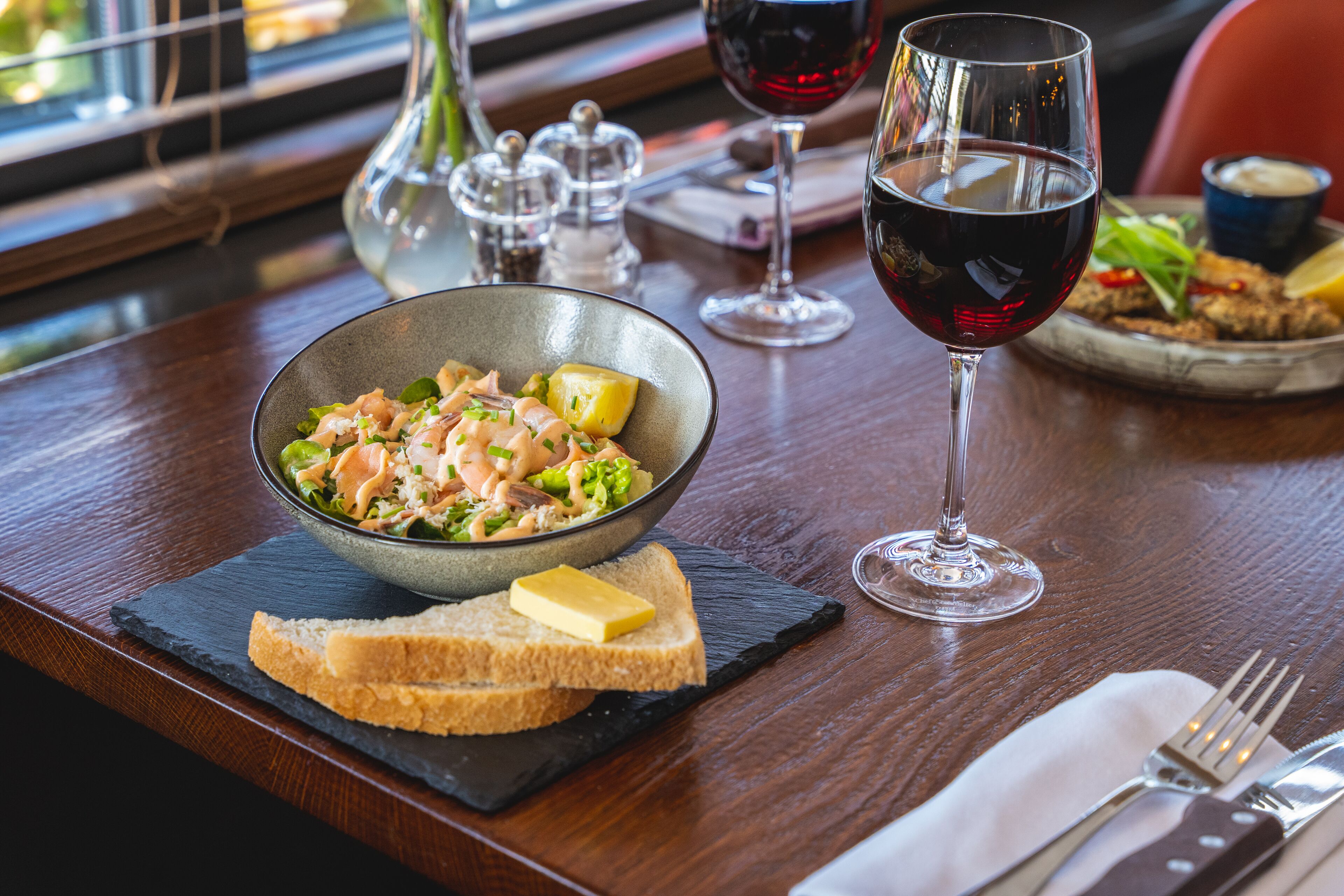 A dining table with a bowl of salad, a glass of red wine, and a plate of food.