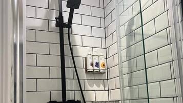 A shower with a glass door, white tiled walls, and a black handheld showerhead.