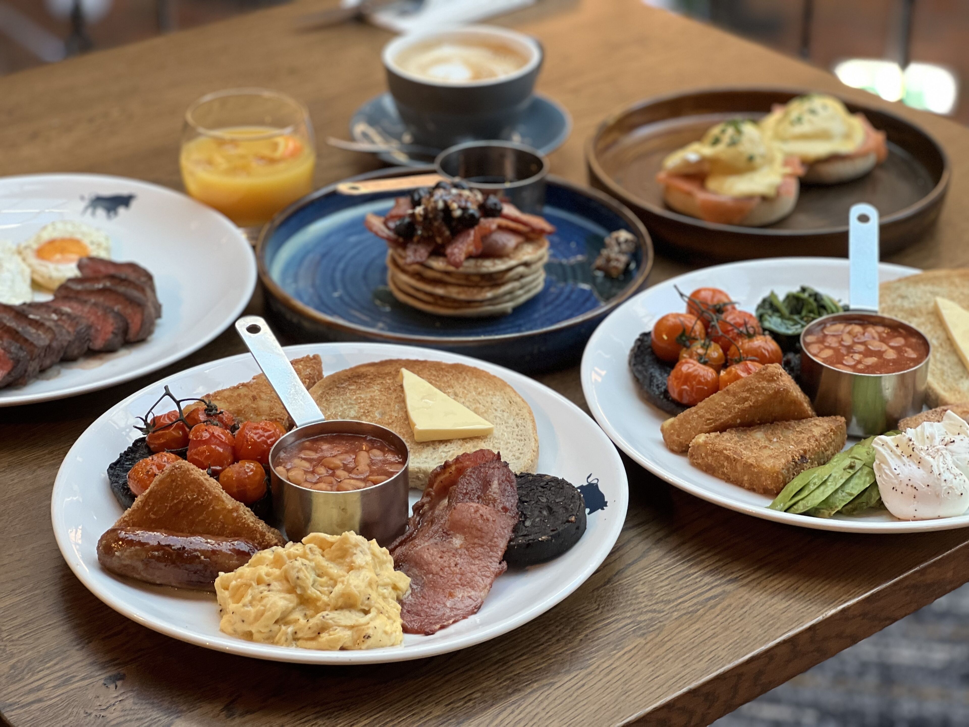 Un bufé de desayuno con diversos platos, incluyendo huevos, tocino, tostadas, frijoles y tomates.