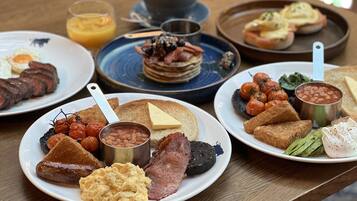 Un bufé de desayuno con diversos platos, incluyendo huevos, tocino, tostadas, frijoles y tomates.