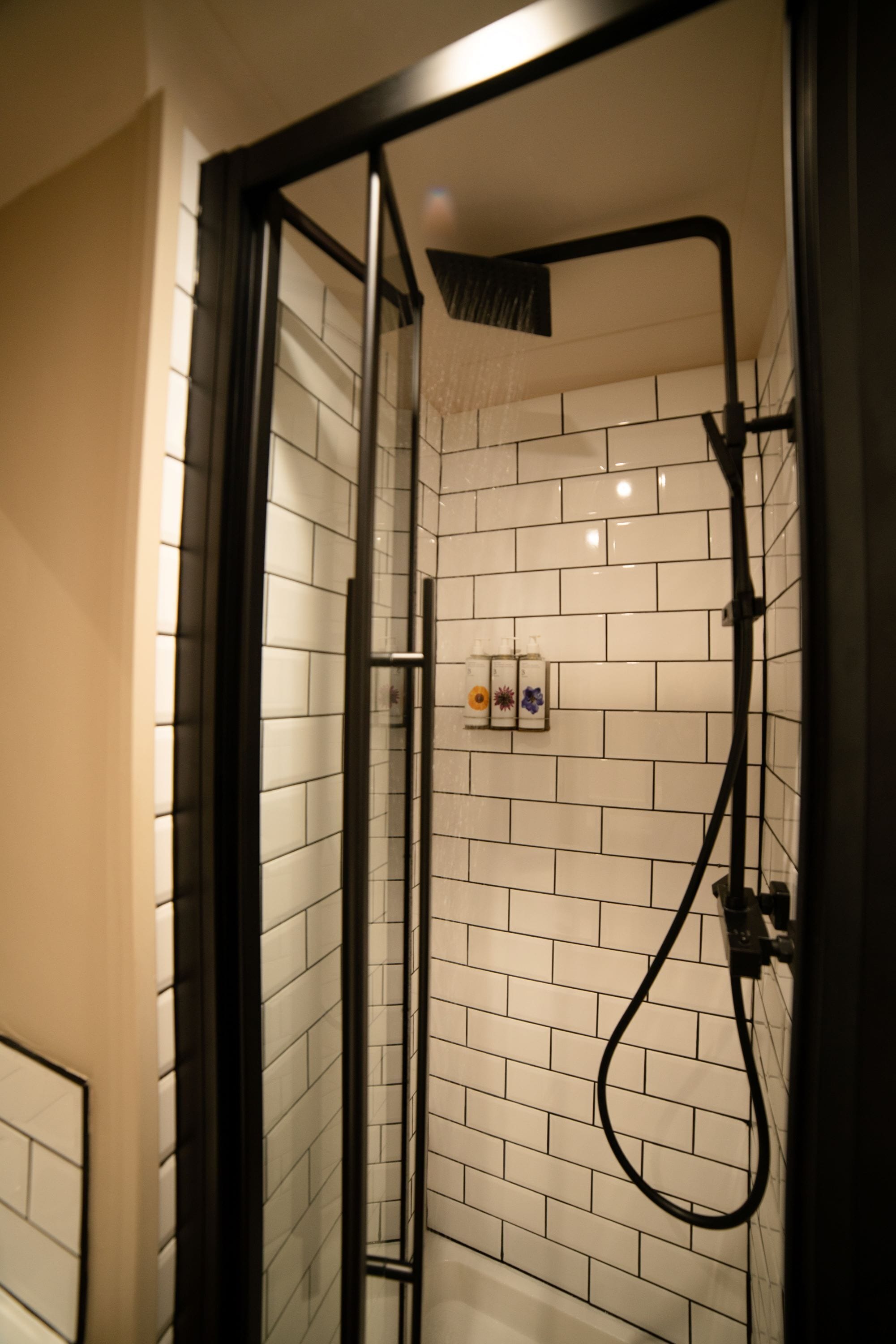 Une douche à l’italienne avec des murs recouverts de carreaux blancs et un cadre noir.