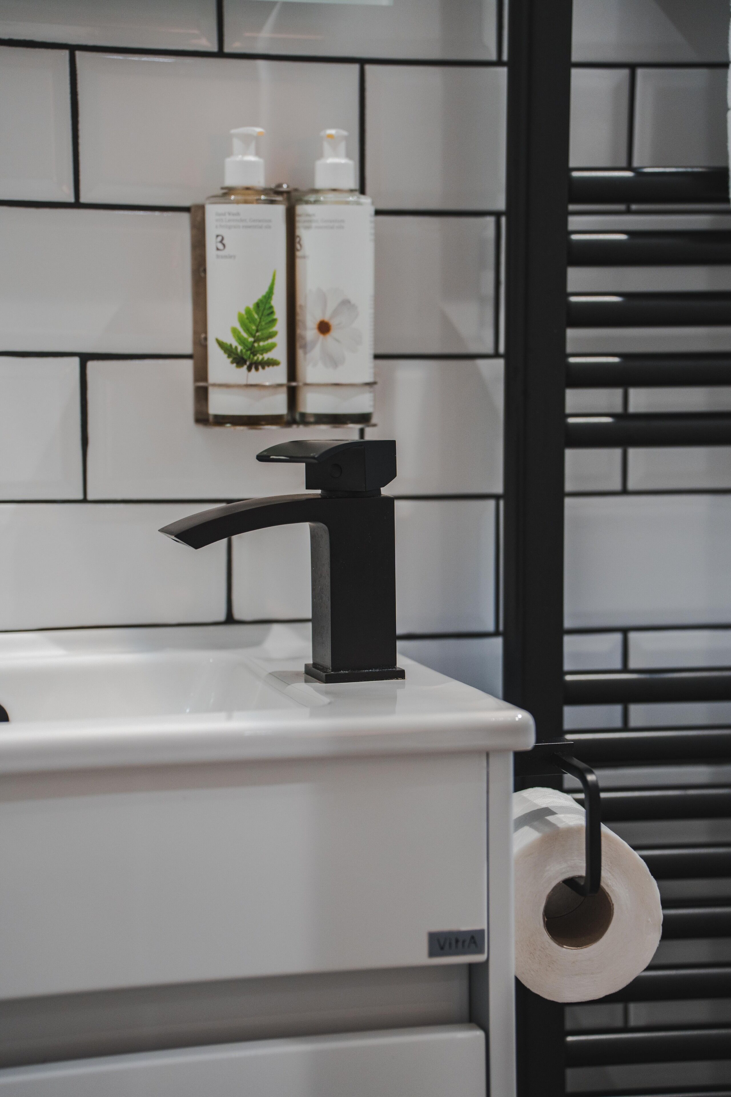 A bathroom with a white sink, black faucet, and two bottles of hand soap on the wall.