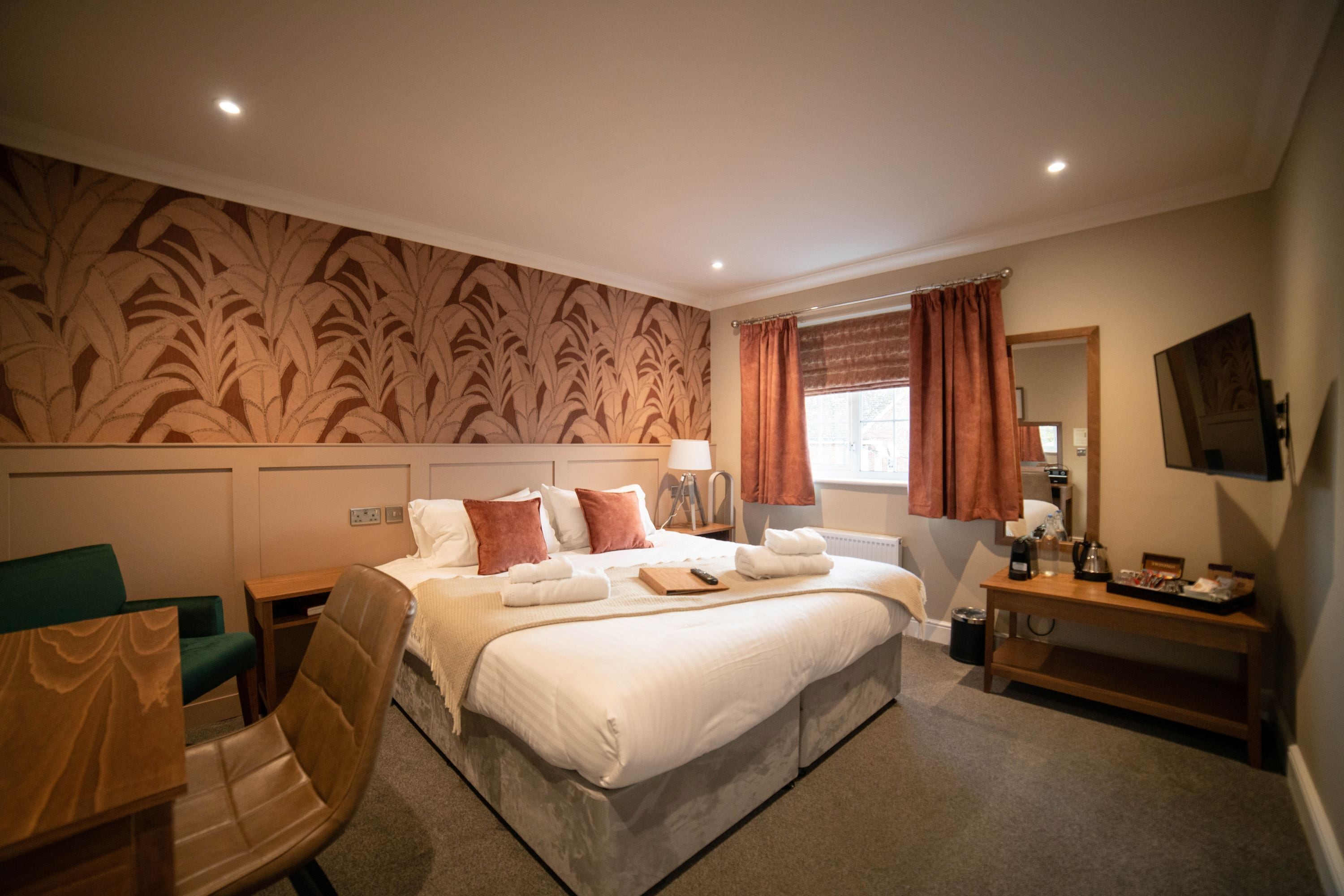 A hotel room with a large bed, a desk, a chair, a mirror, and a television.