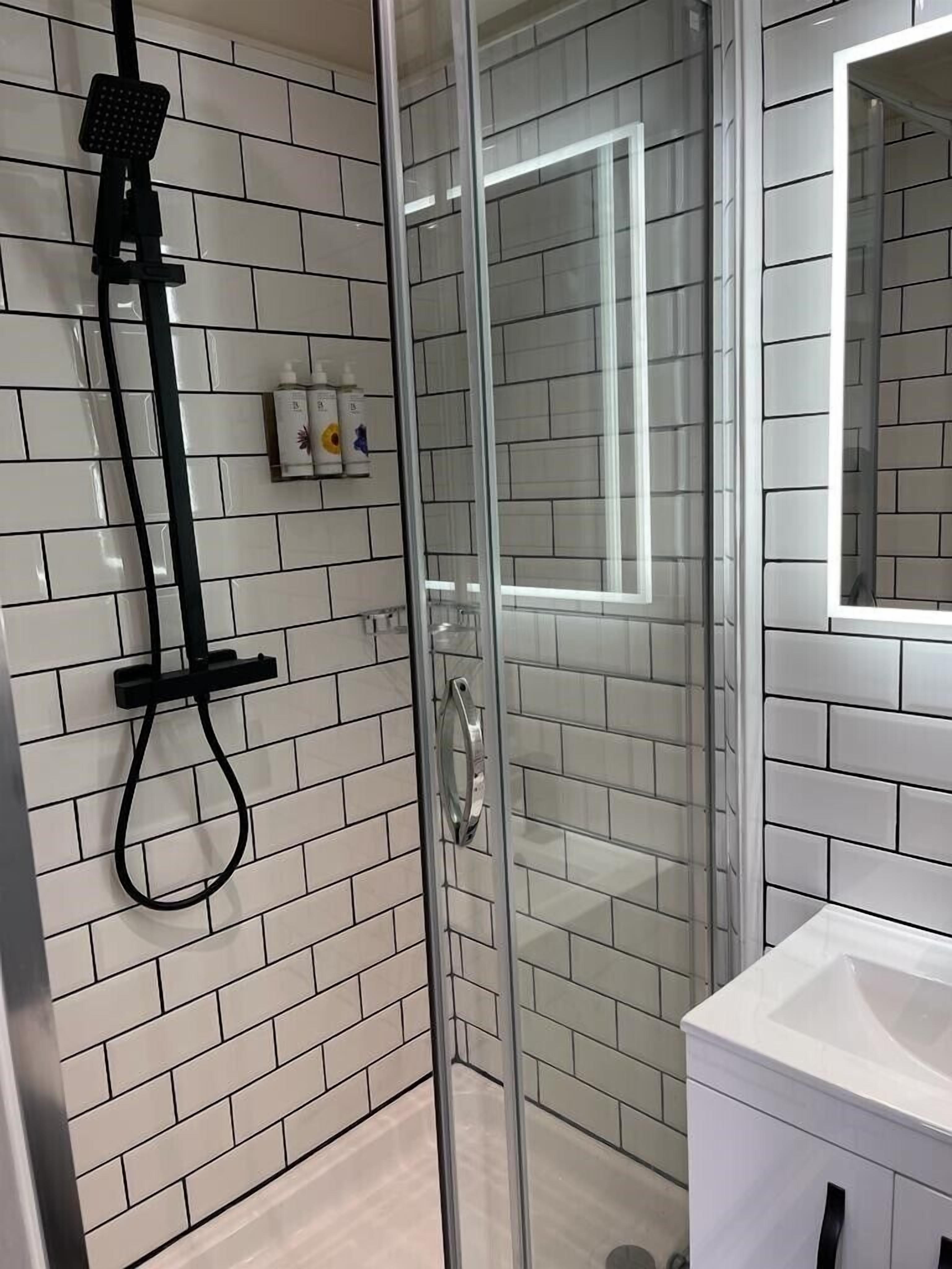 A modern bathroom with white subway tiles, a glass shower enclosure, a handheld showerhead, and a white sink with a mirror above it.