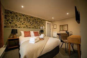 Une chambre d’hôtel avec un grand lit, deux tables de chevet avec des lampes, un bureau, une chaise et un téléviseur fixé au mur.