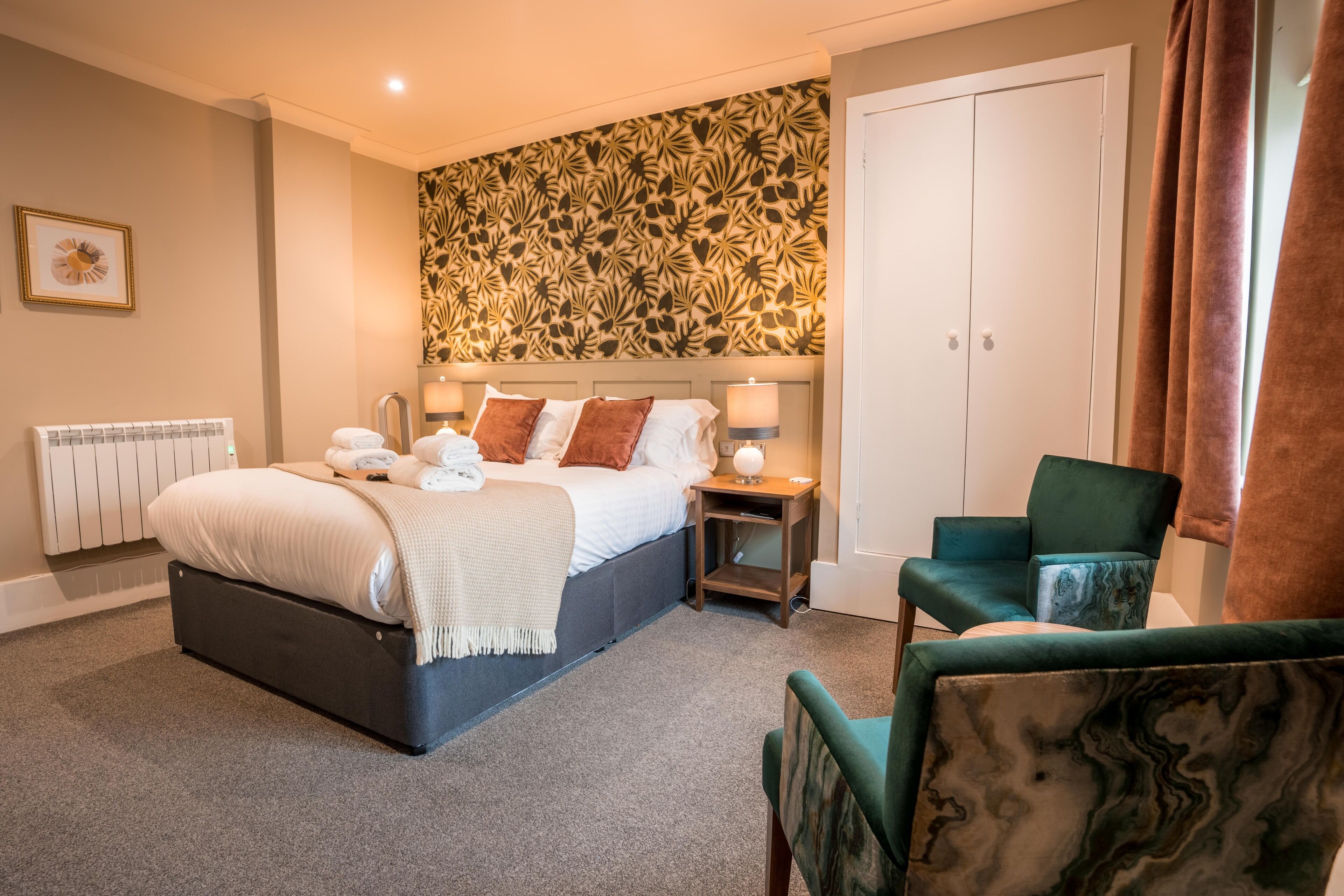 A bedroom with a bed, bedside lamps, a chair, and a patterned wall.